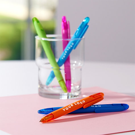 Colorful gel pens in a holder on a desk, a few of the pens are laying on the desk, and all are decorated with your logo