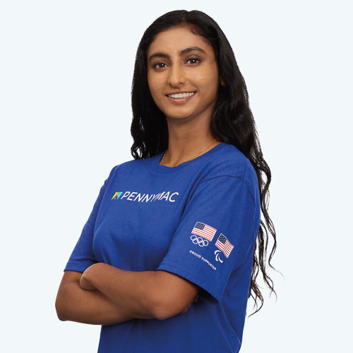 A woman standing with her arms crossed in a co-branded t-shirt with the Pennymac logo across the front of the shirt, and the USA Olympics and USA Paralympics logos on the left arm with the words Proud Supporter