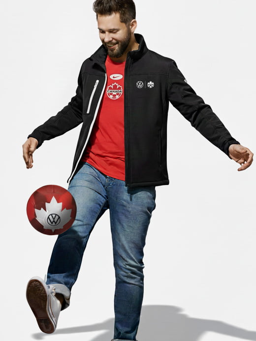 A man wearing VW soccer canada jacket balancing a soccer ball.
