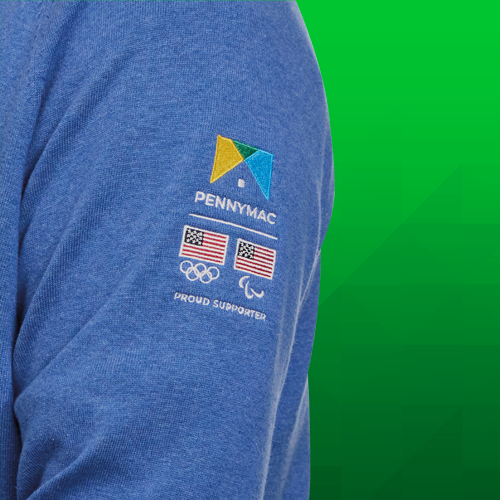 A zoomed in shot of a man wearing a zip pullover, highlighting the Pennymac, USA Olympics, and USA Paralympics logos on the left arm with the words Proud Supporter