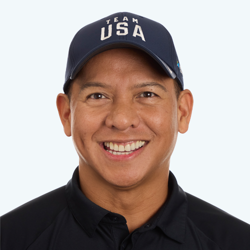 A headshot of a man smiling while wearing a Team USA branded ball cap