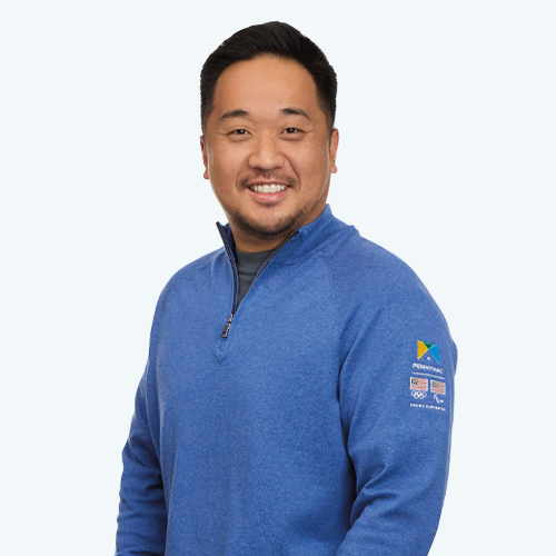 A portrait of a man wearing a zip pullover with the Pennymac, USA Olympics, and USA Paralympics logos on the left arm with the words Proud Supporter