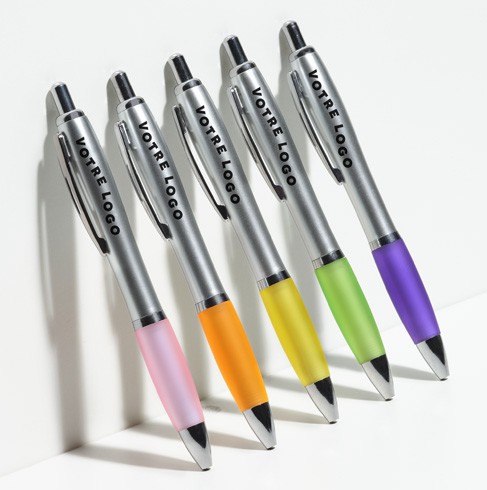 Row of metallic pens with neon grips in pink, orange, yellow, green, and purple — each branded YOUR LOGO, labeled Pens & Writing.