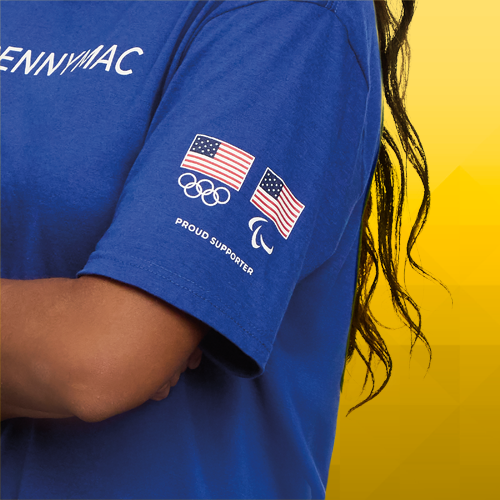 A co-branded t-shirt with the Pennymac logo across the front of the shirt, zoomed in to highlight the USA Olympics and USA Paralympics logos on the left arm with the words Proud Supporter.