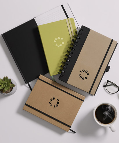 Assorted branded notebooks with Your Logo text, styled with office accessories like glasses, a succulent, and a cup of coffee.
