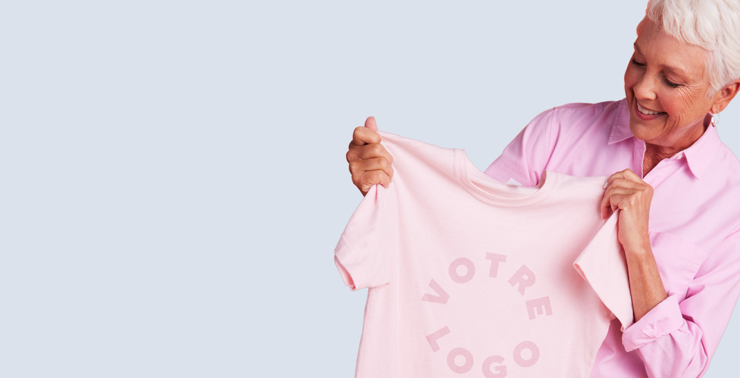 Older woman in pink holds YOUR LOGO tee with ORDER ONE... OR MORE! speech bubble and Deals button — for promo deals